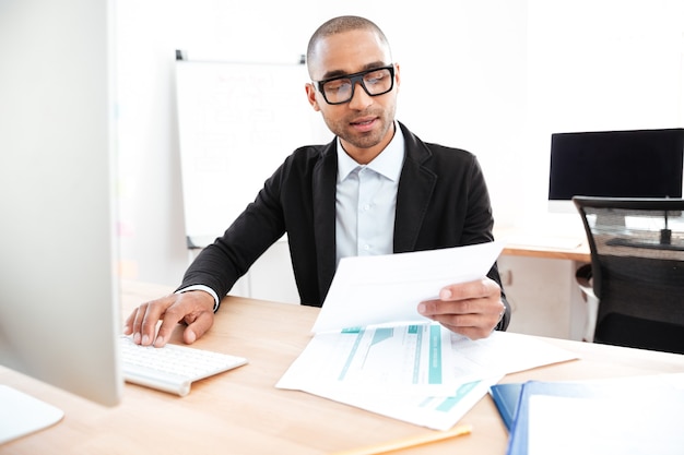 Beau jeune homme d'affaires intelligent travaillant avec des documents au bureau